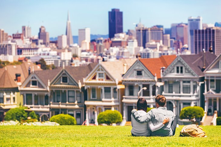 一对情侣在阿拉莫公园放松，俯瞰着彩绘女士的房子和旧金山市中心